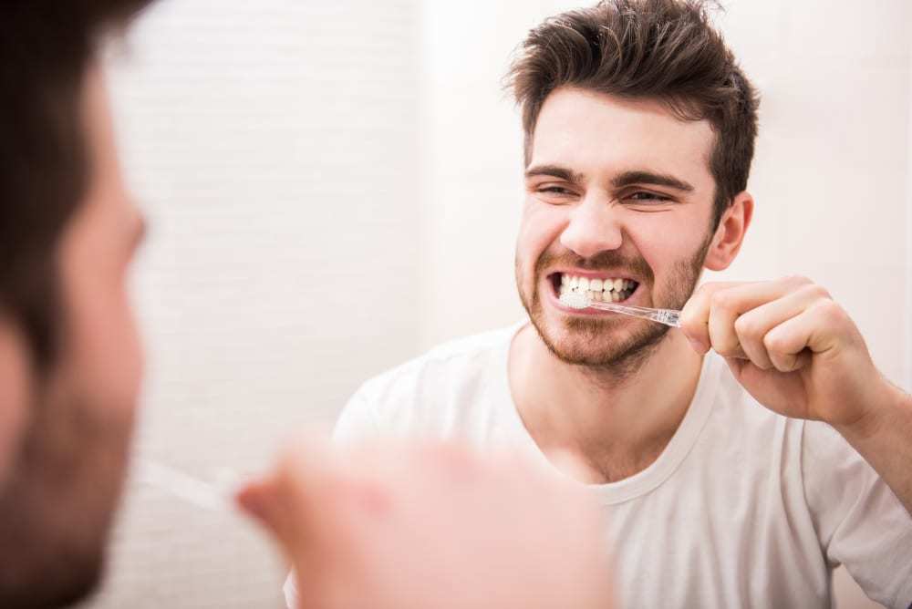 joven-mirándose-en-el-espejo-mientras-se-lava-los-dientes-para-quitarse-el-mal-aliento